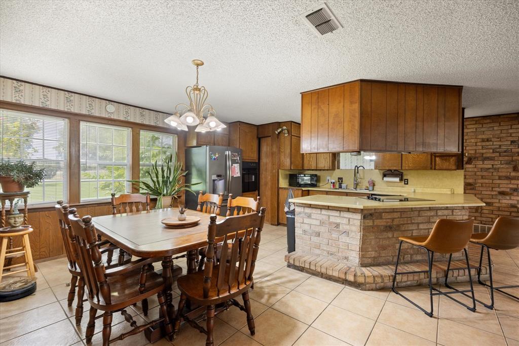 4210 Waples Road Granbury, TX 76049 - Photo 20 of 37 Kitchen and dining area featuring tile flooring, wood-finish paneling, and an exposed brick accent wall