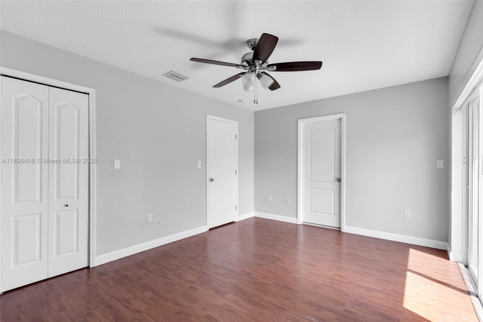 2883 Southwest 129th Terrace, Unit 2883 Miramar, FL 33027 - Photo 11 of 18 an empty room with wooden floor a ceiling fan and windows