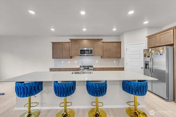 a kitchen with granite countertop a refrigerator a stove a sink and chairs
