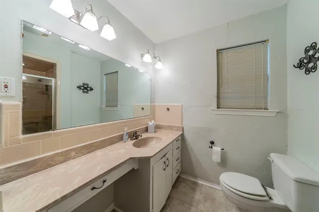 a bathroom with a granite countertop sink a toilet a mirror and shower