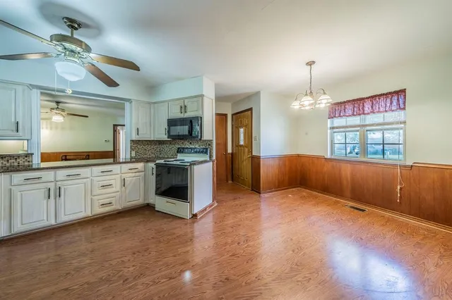 an empty room with wooden floor chandelier fan and windows