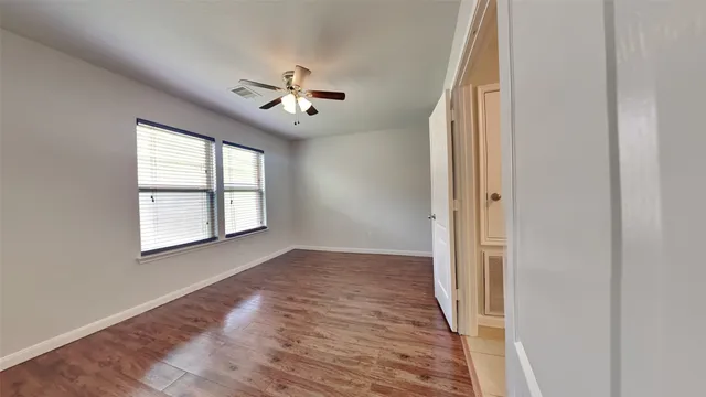 an empty room with wooden floor chandelier fan and windows
