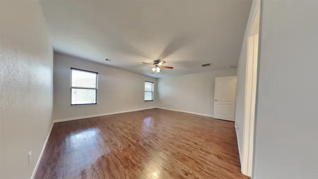 an empty room with wooden floor chandelier fan and windows