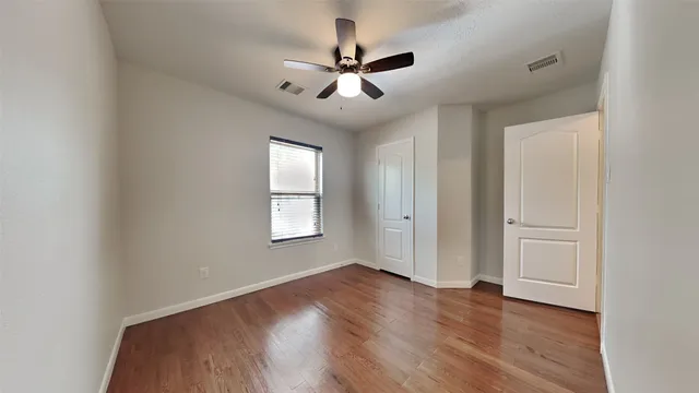 an empty room with wooden floor fan and windows