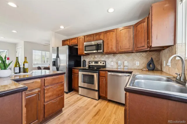a kitchen with stainless steel appliances granite countertop a refrigerator a sink dishwasher a stove top oven a refrigerator with wooden cabinets and floor