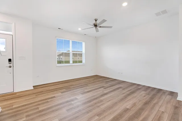 an empty room with wooden floor ceiling fan and windows