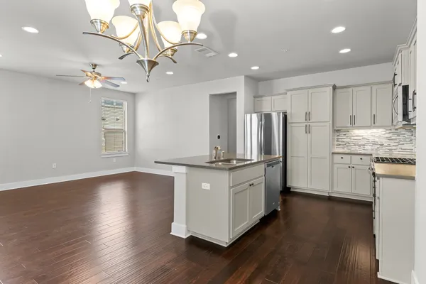 a kitchen with stainless steel appliances granite countertop a sink a stove a refrigerator and island with wooden floor