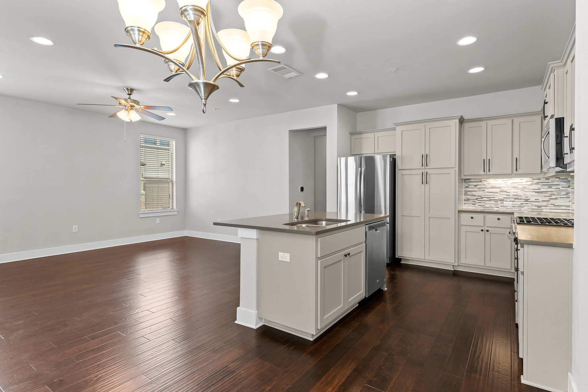 13800 Lyndhurst Street, Unit 211 Austin, TX 78717 - Photo 13 of 40 Kitchen featuring a chandelier, an island with sink, tasteful backsplash, and dark wood finished floors