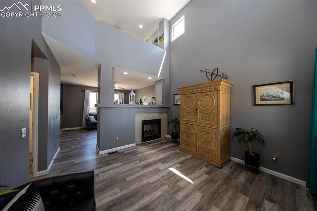 7511 Coffee Road Peyton, CO 80831 - Photo 5 of 38 Living area with wood finished floors, a high ceiling, baseboards, recessed lighting, and a tiled fireplace