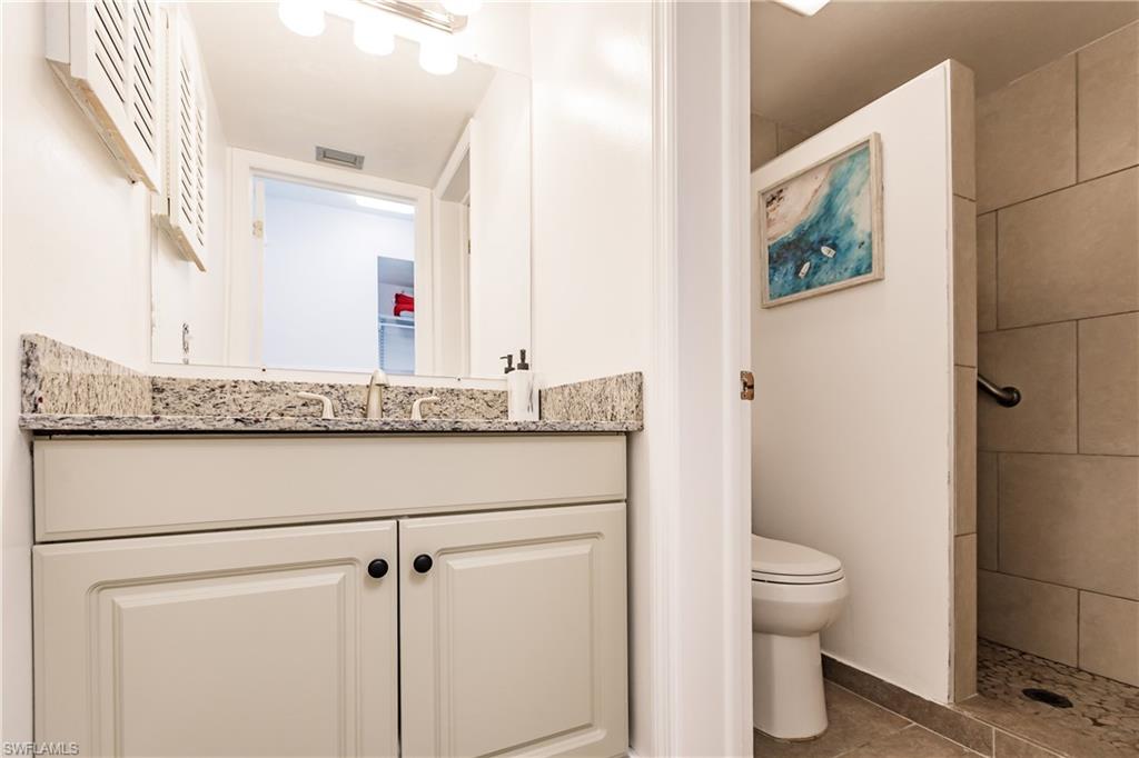 600 Neapolitan Way, Unit 152 Naples, FL 34103 - Photo 11 of 41 a bathroom with a granite countertop sink a toilet and a mirror