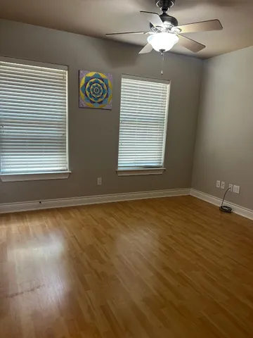 an empty room with wooden floor fan and windows