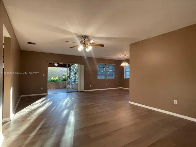 an empty room with wooden floor chandelier and windows