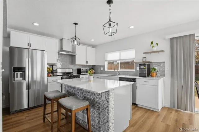 a kitchen with stainless steel appliances granite countertop a refrigerator a sink dishwasher a stove and white cabinets with wooden floor