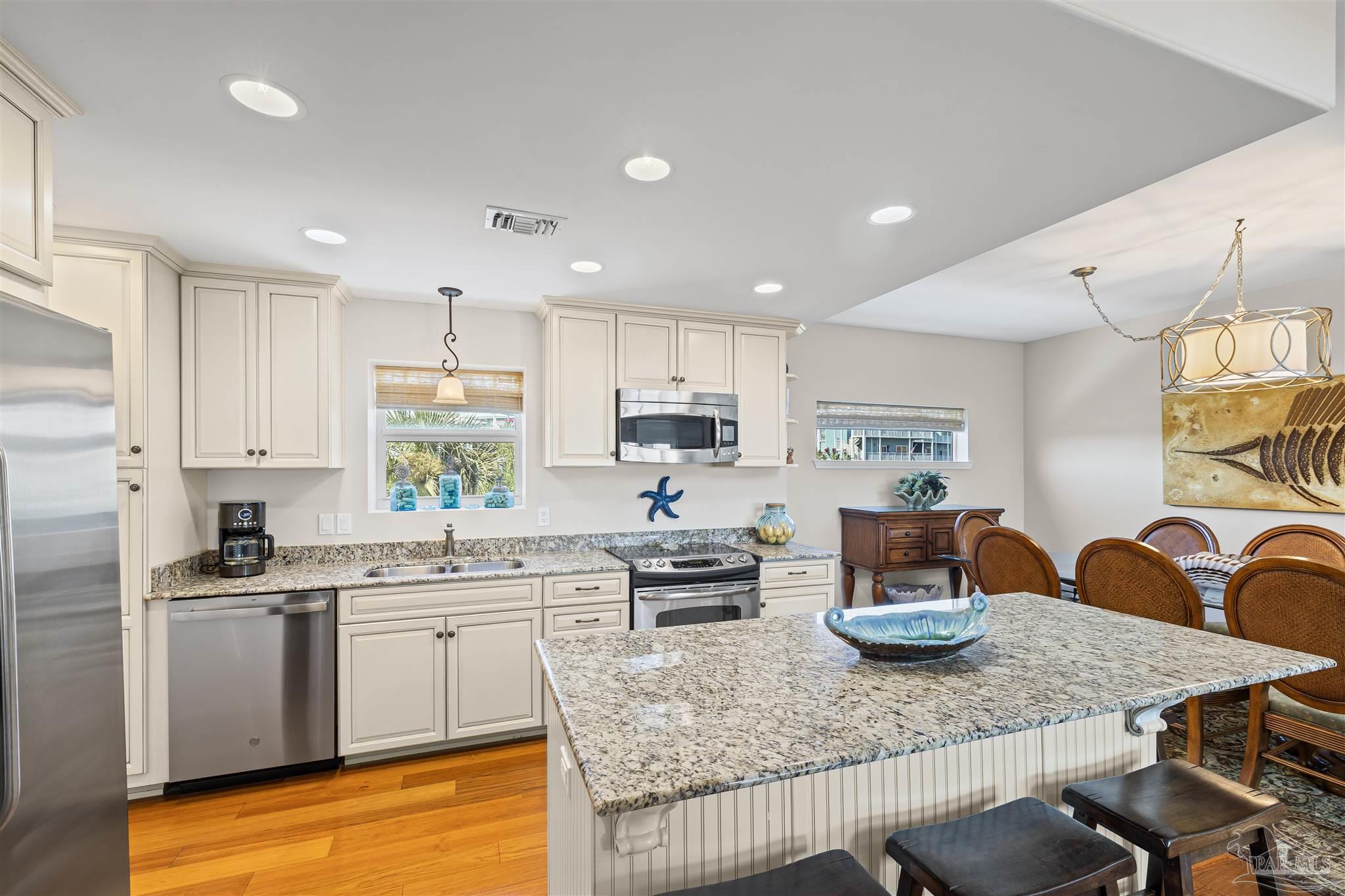 1299 Fort Pickens Road, Unit 10 Pensacola Beach, FL 32561 - Photo 11 of 58 a kitchen with stainless steel appliances granite countertop a sink a stove a kitchen island with chairs and white cabinets