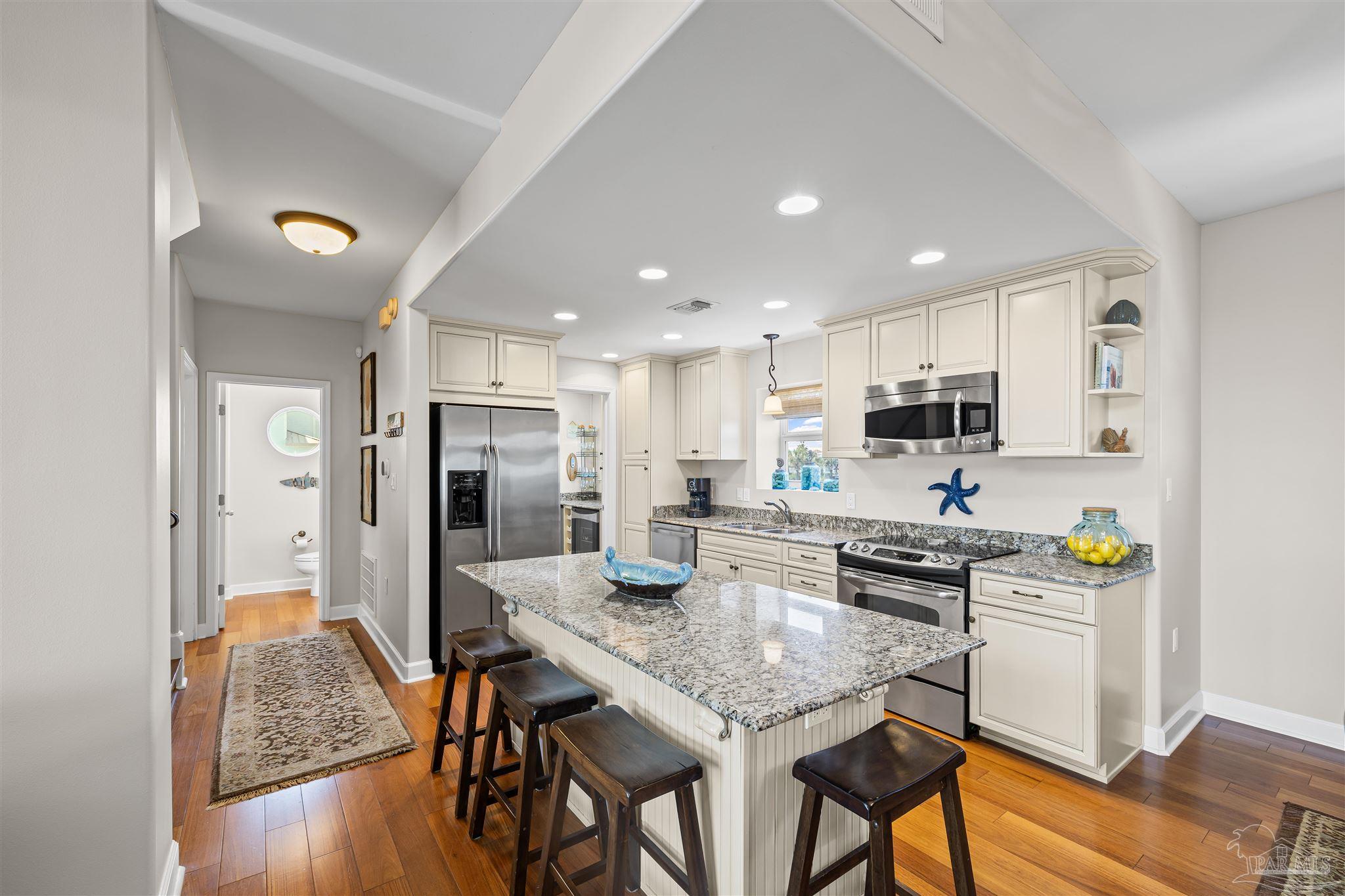 1299 Fort Pickens Road, Unit 10 Pensacola Beach, FL 32561 - Photo 12 of 58 a kitchen with stainless steel appliances granite countertop a stove top oven a refrigerator a sink and white cabinets with wooden floor