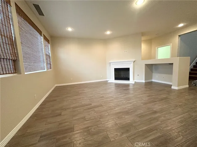 an empty room with wooden floor fireplace and windows