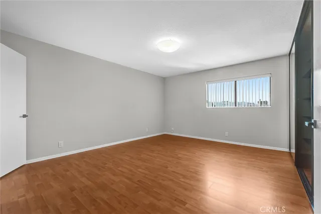 a view of an empty room with a kitchen and entryway with wooden floor