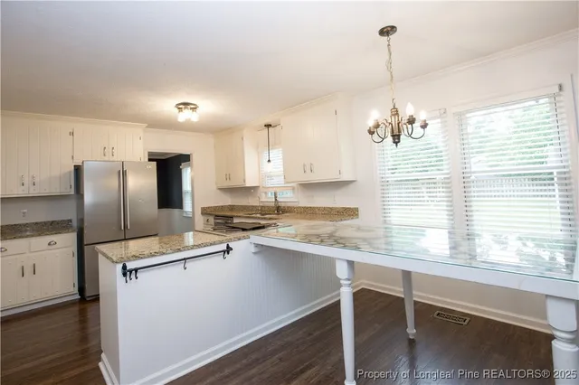 a kitchen with stainless steel appliances granite countertop a sink a stove a refrigerator cabinets and a dining table with wooden floor