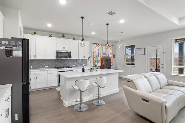a large white kitchen with stainless steel appliances kitchen island granite countertop a table chairs and a refrigerator