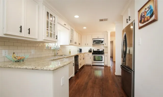 a kitchen with stainless steel appliances granite countertop a refrigerator a sink dishwasher a stove and white countertops with wooden floor