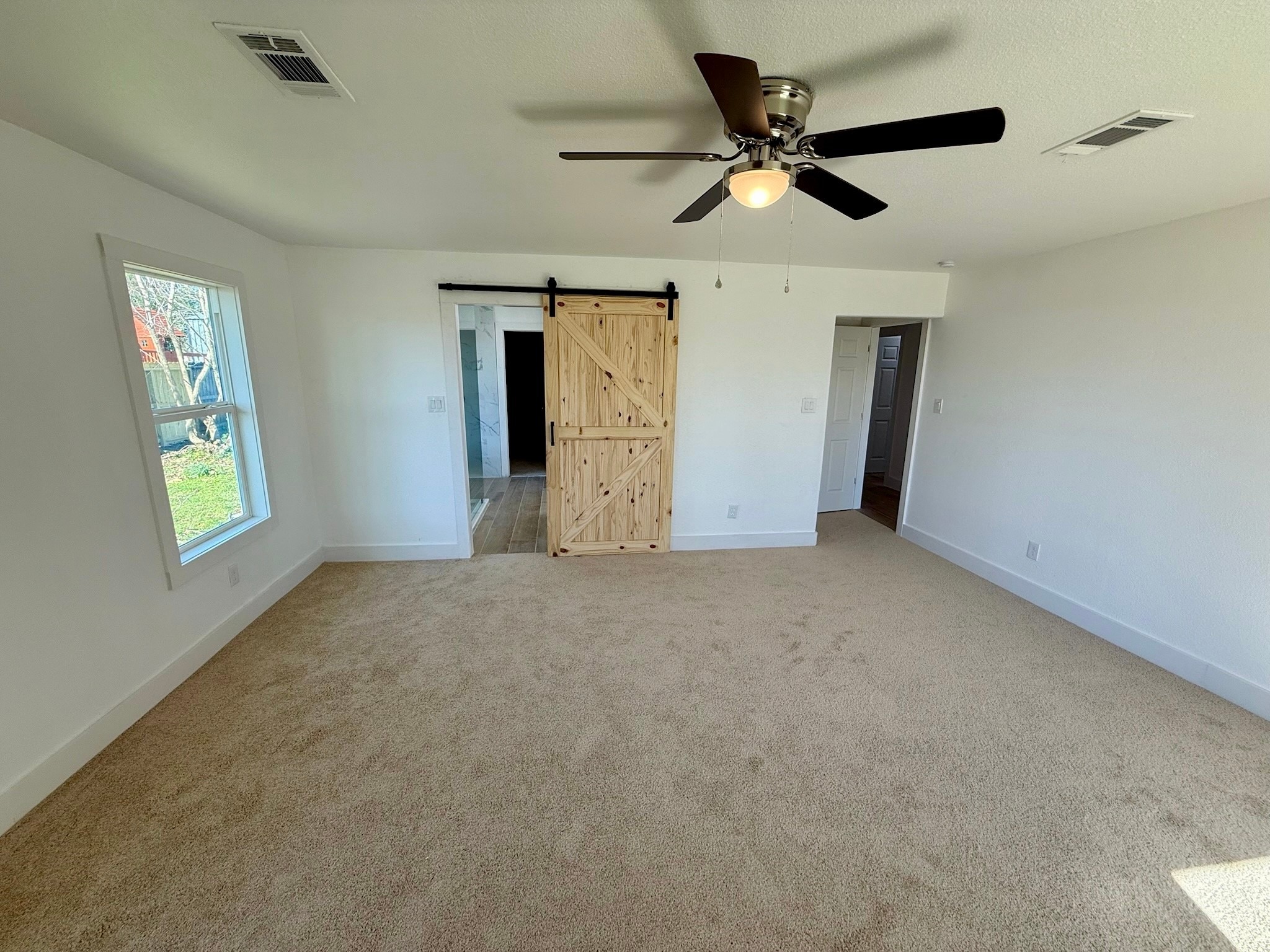 1214 Main Street Alvin, TX 77511 - Photo 11 of 18 This spacious Primary bedroom features neutral carpeting, a ceiling fan with light, ample natural light from a large windows, and a rustic sliding barn door, creating a cozy and inviting atmosphere.