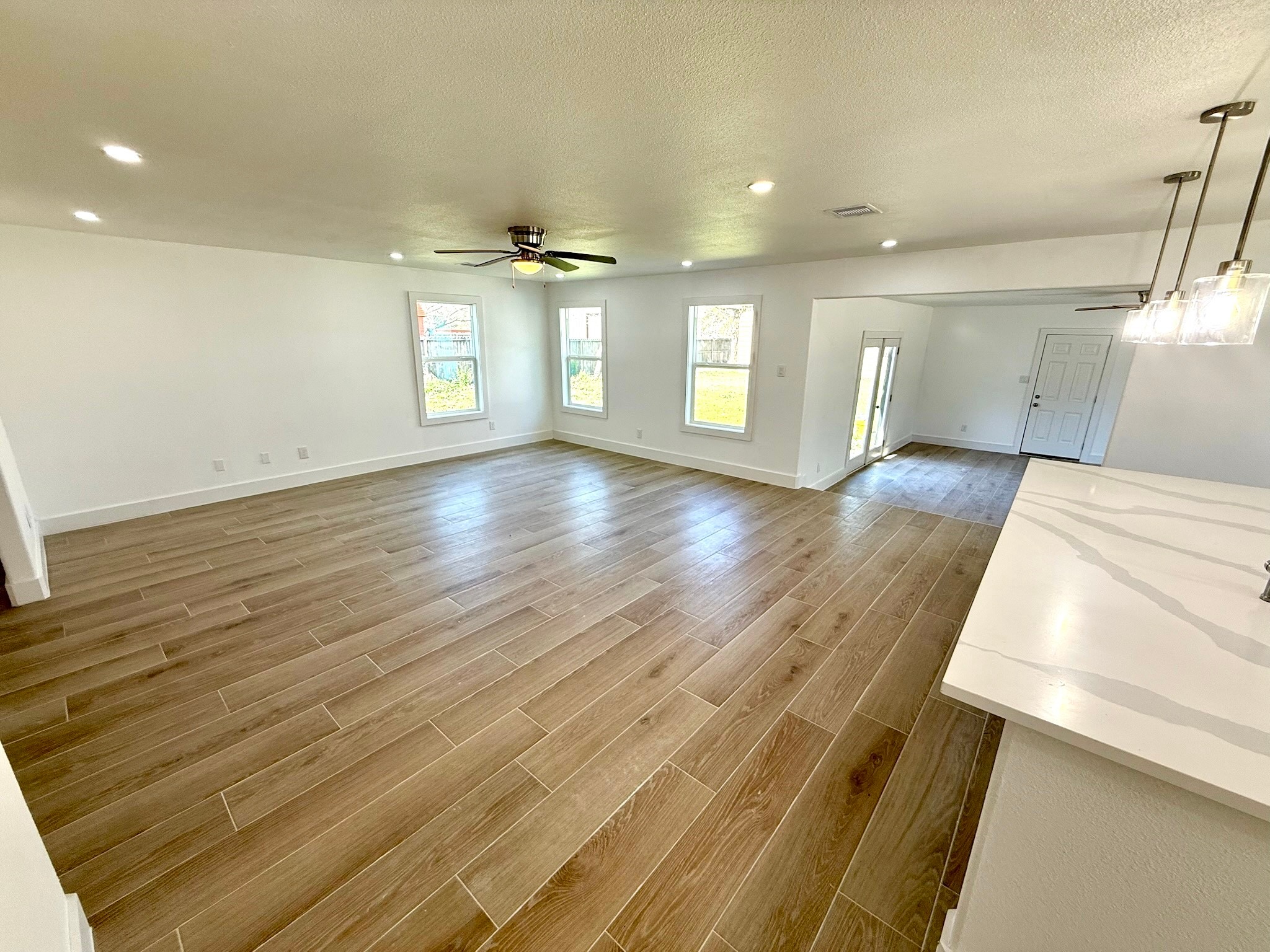 1214 Main Street Alvin, TX 77511 - Photo 8 of 18 Spacious, bright living room with wood-look flooring, neutral walls, large windows, and a ceiling fan, offering a modern and inviting atmosphere.