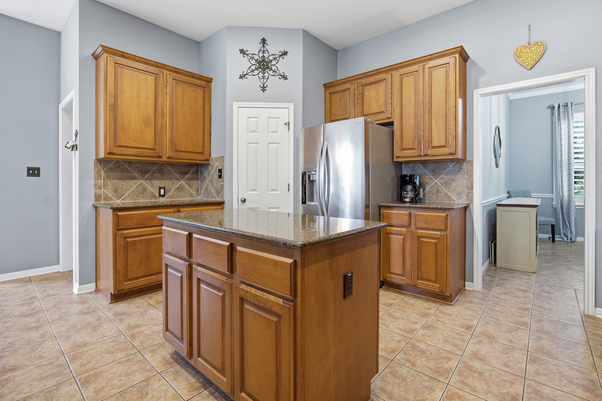 2204 Rio Mesa Drive Austin, TX 78732 - Photo 16 of 40 The kitchen features a functional island with a granite countertop, wood cabinetry, stainless steel refrigerator, and tiled flooring