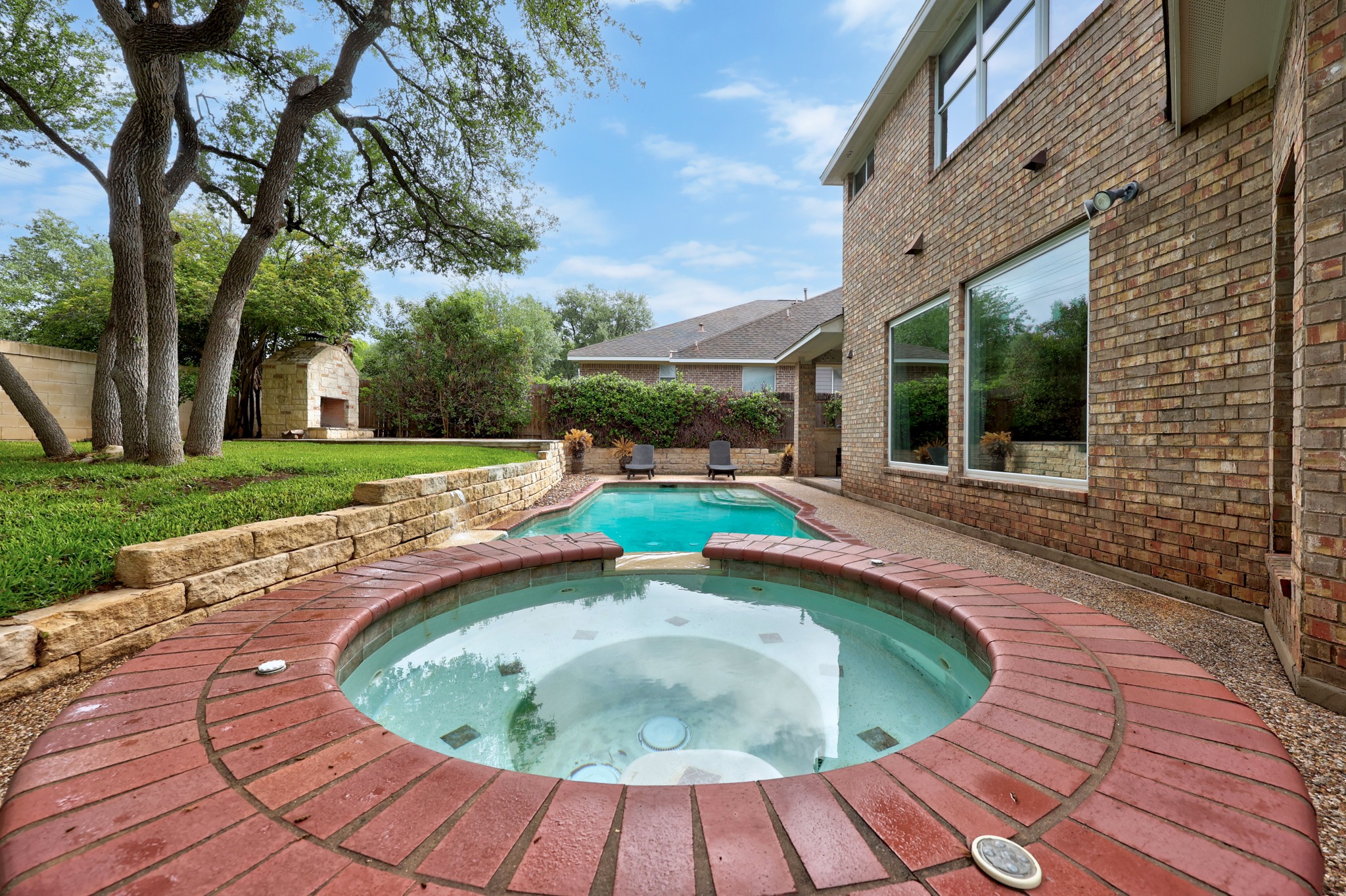 2204 Rio Mesa Drive Austin, TX 78732 - Photo 37 of 40 The property features a backyard with a circular hot tub surrounded by brick paving, and a swimming pool with two lounge chairs