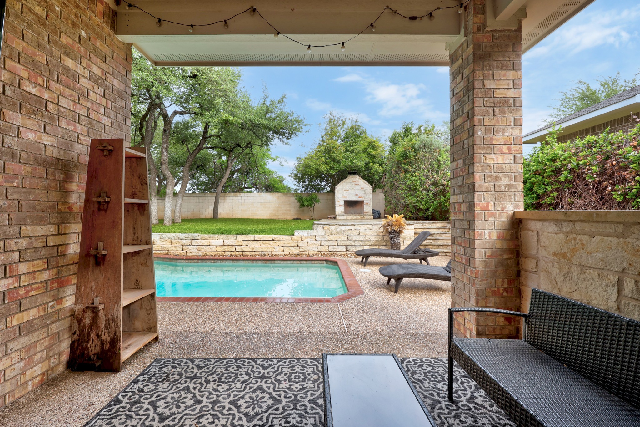 2204 Rio Mesa Drive Austin, TX 78732 - Photo 38 of 40 The property features a patio area with a brick exterior and a string of overhead lights, overlooking a swimming pool with a stone wall surround