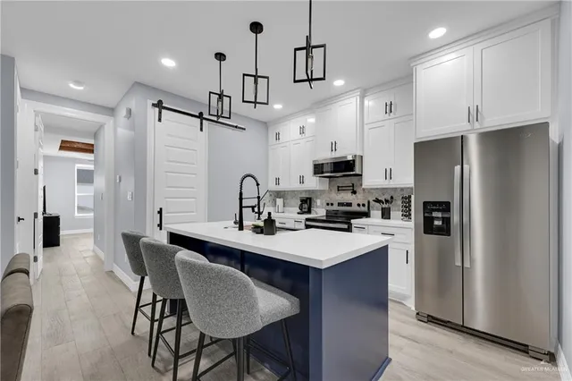 a kitchen with stainless steel appliances a sink a stove a refrigerator a center island and chairs