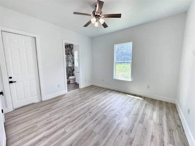 an empty room with wooden floor chandelier fan and windows