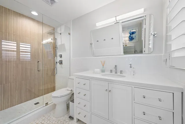 a bathroom with a toilet a sink a glass door a shower a and mirror