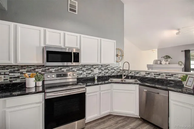 a white kitchen with granite countertop a stove top oven microwave and cabinets