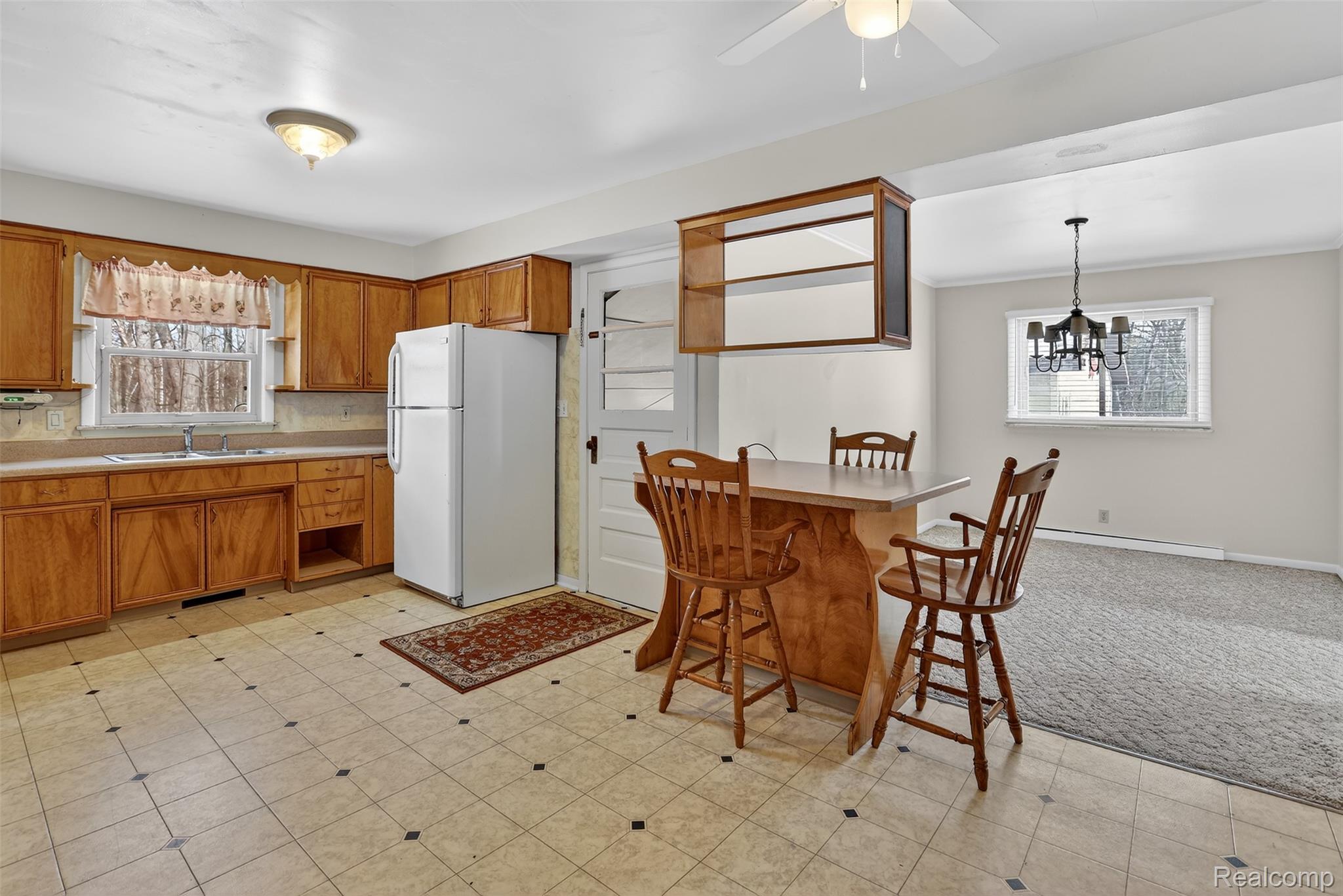 3241 Curtis Road Birch Run, MI 48415 - Photo 16 of 47 Kitchen with brown cabinets, freestanding refrigerator, light countertops, light flooring, and hanging light fixtures