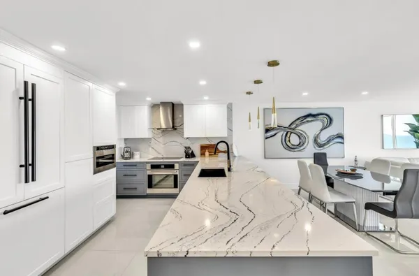 a kitchen with stainless steel appliances kitchen island granite countertop a stove a sink a refrigerator and white cabinets with wooden floor