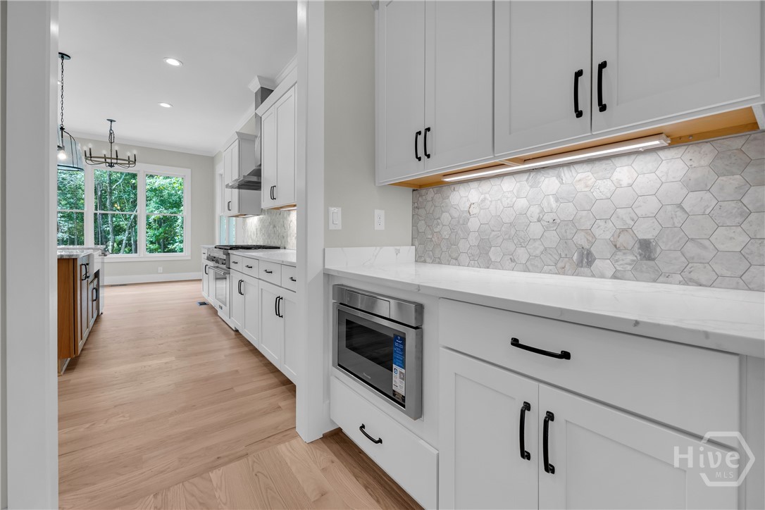 2476 St Martin Way Monroe, GA 30656 - Photo 13 of 75 Kitchen featuring bright white cabinetry with black hardware, white countertops, built-in microwave, hexagonal tile backsplash with under-cabinet lighting, and wood-finish flooring