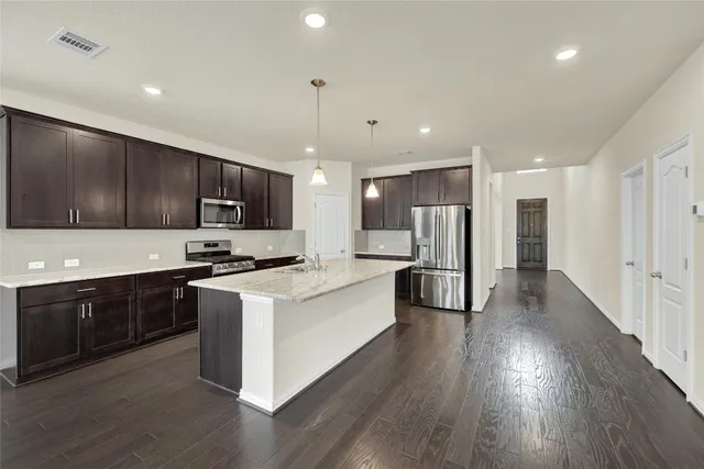 a large kitchen with stainless steel appliances granite countertop a large center island a stove a refrigerator white cabinets and wooden floor