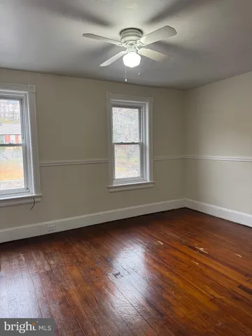 an empty room with wooden floor chandelier fan and windows