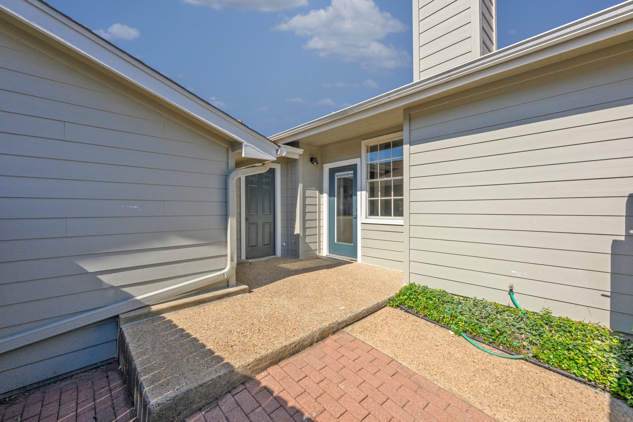 6501 Brush Country Road, Unit 120 Austin, TX 78749 - Photo 23 of 26 Exterior features include light gray horizontal siding and a red brick paver pathway leading to an exposed aggregate concrete walkway