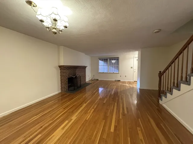 a view of an empty room with wooden floor fireplace and a window