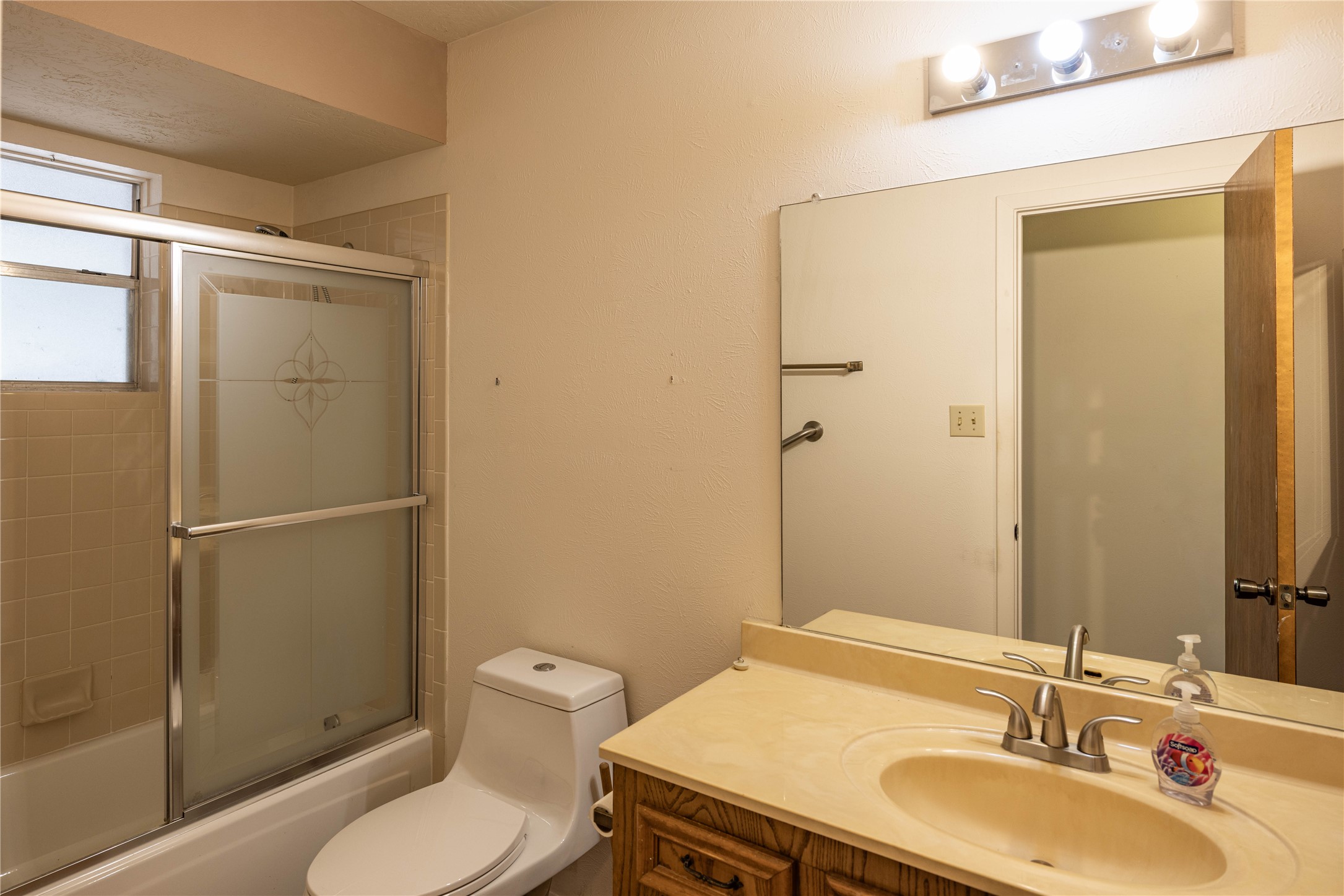 2501 Fischer Store Road Wimberley, TX 78676 - Photo 11 of 23 Bathroom featuring a shower-tub combination with sliding glass doors, a single vanity with a built-in sink, and a wall-mounted mirror
