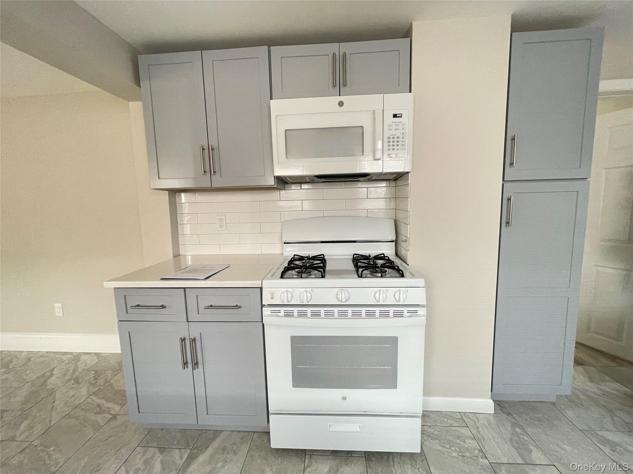 89 2nd Street, Unit 1 New Rochelle, NY 10801 - Photo 5 of 13 Kitchen featuring gray cabinetry, white appliances, backsplash, and light countertops