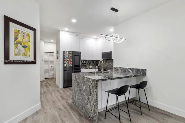 a view of a kitchen with kitchen island a dining table chairs stainless steel appliances and cabinets