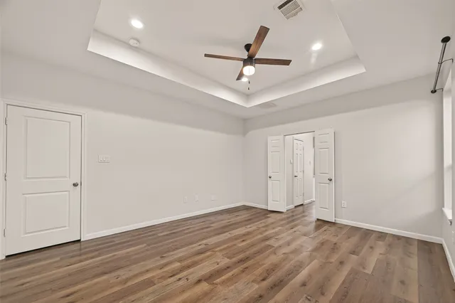 a view of an empty room with wooden floor and a ceiling fan