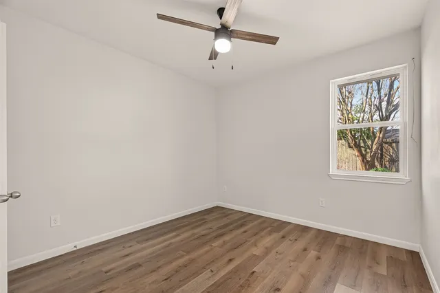 an empty room with wooden floor ceiling fan and windows
