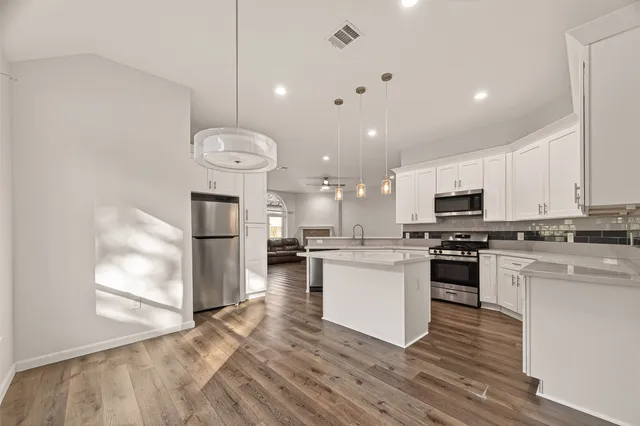 a kitchen with stainless steel appliances granite countertop a refrigerator a stove top oven a sink dishwasher and white cabinets with wooden floor