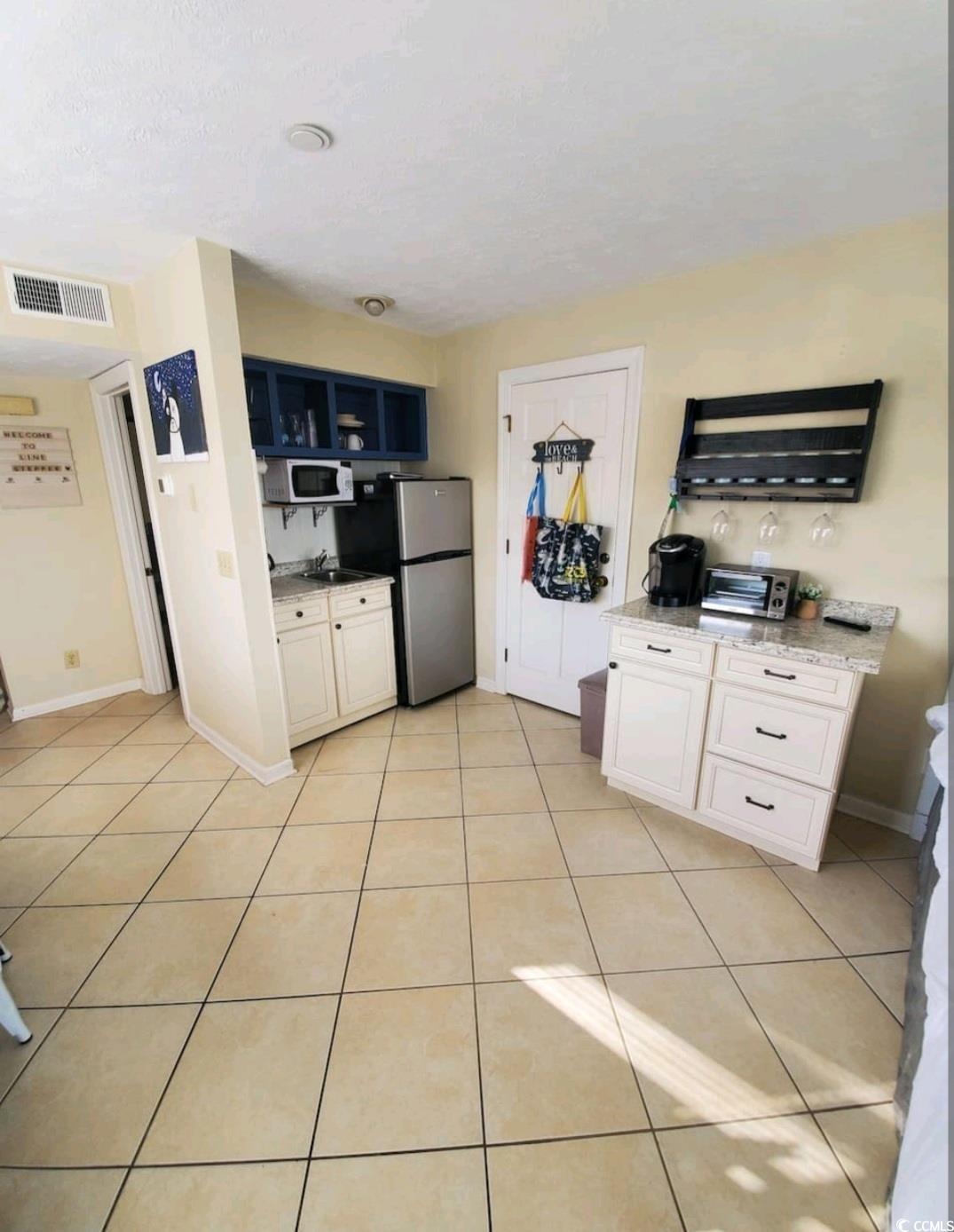 2000 South Ocean Boulevard, Unit V207AB Myrtle Beach, SC 29577 - Photo 3 of 11 Kitchen with open shelves, light tile patterned floors, white cabinets, white microwave, and freestanding refrigerator
