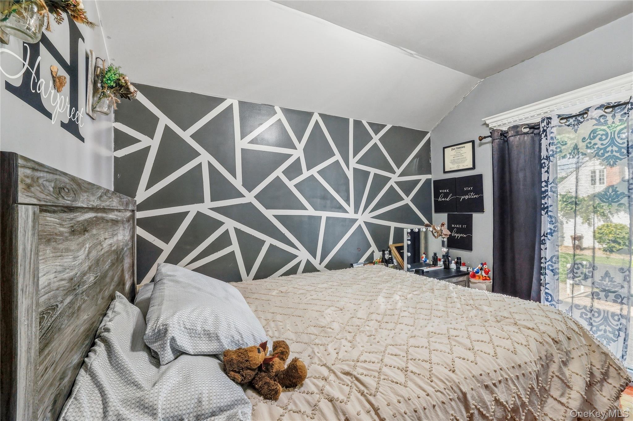 83-39 252nd Street Queens, NY 11426 - Photo 8 of 26 Bedroom featuring a wood-finish headboard, a geometric accent wall, and a window with decorative curtains