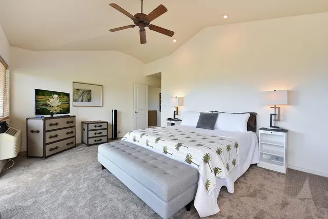 a spacious bedroom with a bed a couch and a flat tv screen on dresser