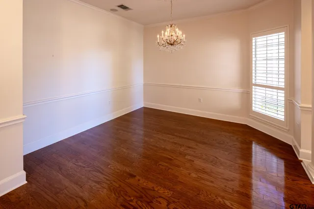 an empty room with wooden floor chandelier and windows